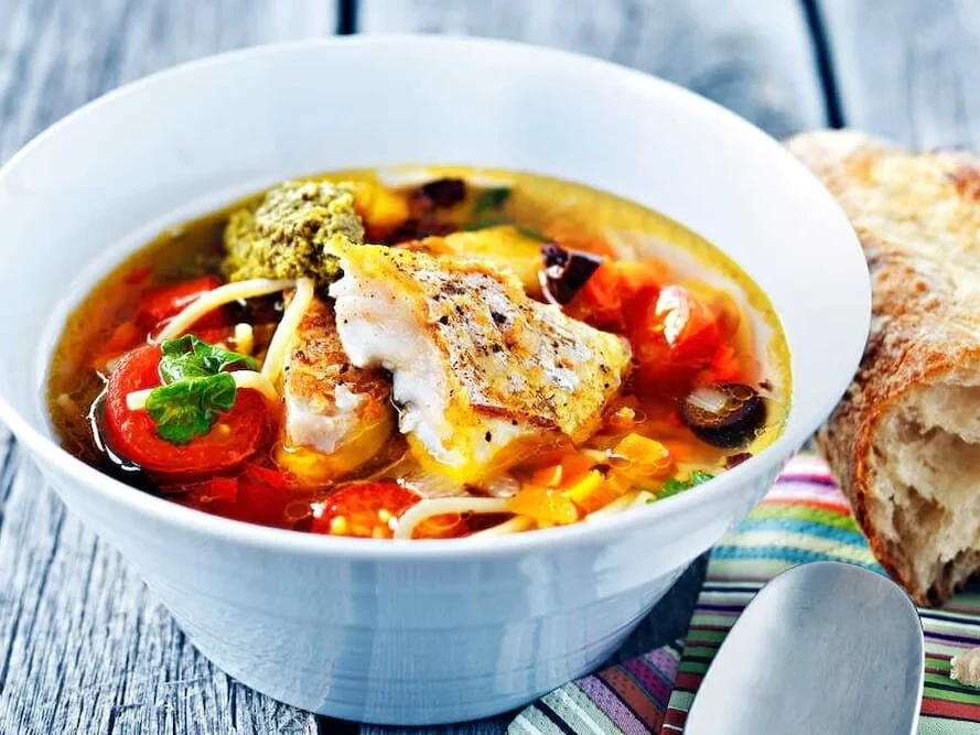 A bowl with veggies and fish floating on the top.