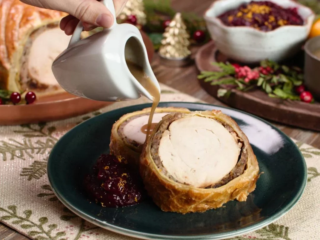 turkey wellington with cranberry sauce and gravy being poured over it