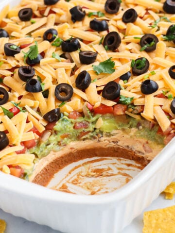 Baking dish of 7 Layer Taco Dip topped with cilantro and black olives.