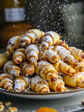 Plate of Apricot Rugelach being sprinkled with powdered sugar.