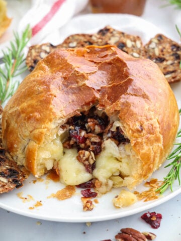Baked Brie in Puff Pastry with brie, pecans, and cranberries spilling out.