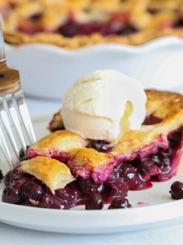 Blueberry Pie slice with a scoop of vanilla ice cream on top on a white plate with a fork