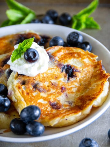 Blueberry Ricotta Pancakes on a plate with blueberries and whipped cream.