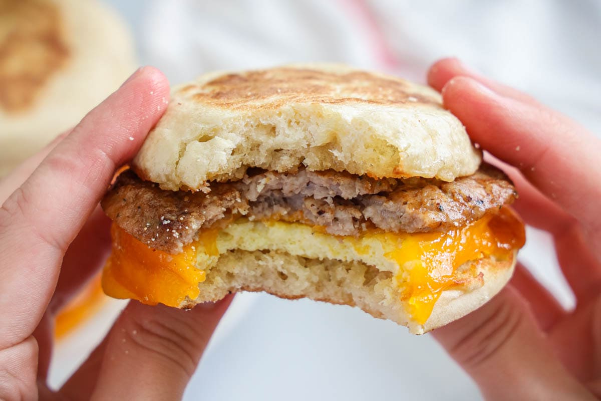 Hands holding a Breakfast Sandwich, one bite missing.
