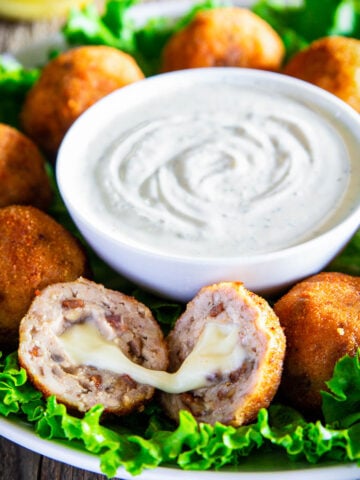 Chicken Croquettes around a bowl of ranch dressing, one split in half to show the gooey cheese.