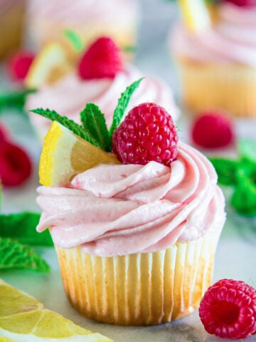 Lemon Raspberry Cupcake topped with lemon, mint, and a raspberry with more nearby.