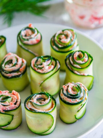 Plate of Smoked Salmon Appetizers made with rolled cucumber slices, salmon, cream cheese, and dill.