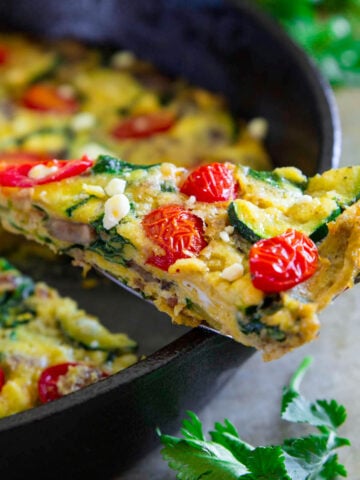 Close up of a slice of Zucchini Frittata being lifted from a cast iron skillet.