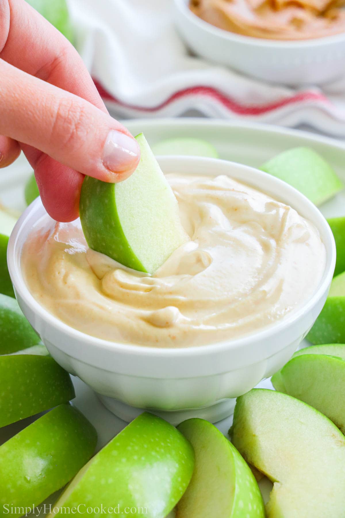 A hand dipping an apple slice into a bowl of Peanut Butter Yogurt Dip.
