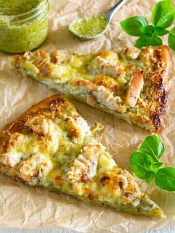 Slices of Chicken Pesto Pizza with pesto and basil nearby