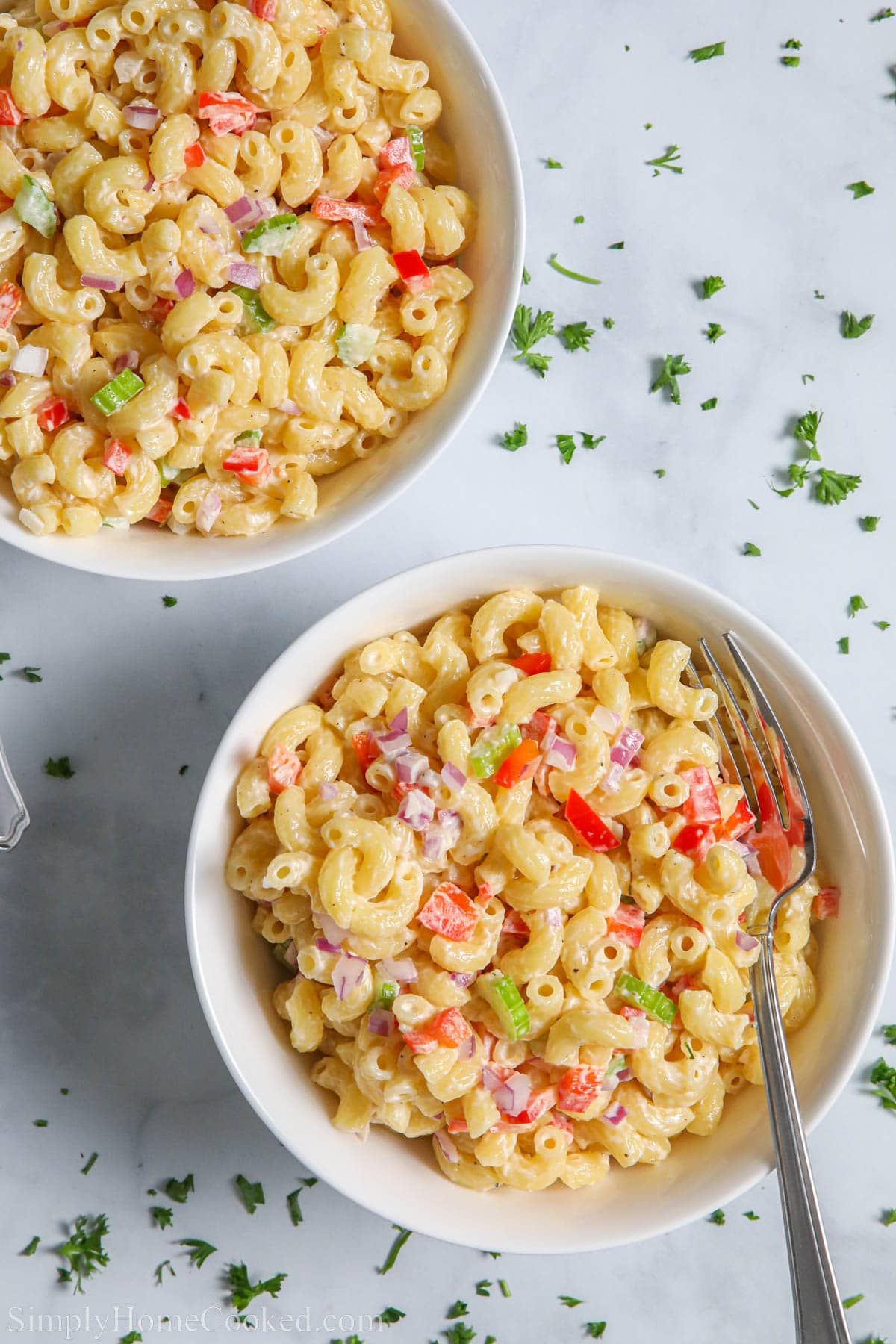 Two bowls of Creamy Pasta Salad with elbow macaroni and diced vegetables with forks and chopped parsley sprinkled nearby.