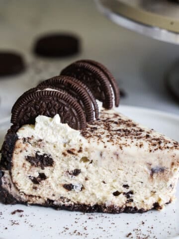 Front view of a slice of Easy Oreo Cheesecake with 3 Oreos on top and crumbs on the white plate.