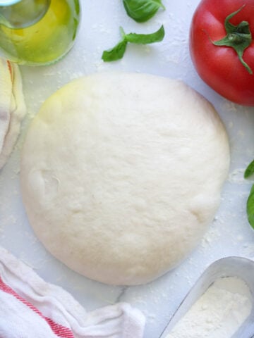 Homemade Pizza Dough with basil, tomato, and flour nearby.