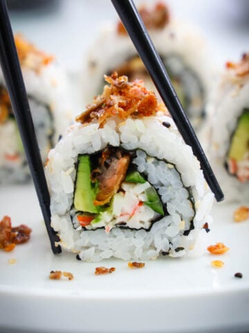 Salmon Skin Roll cut and topped with crispy salmon skins being picked up by chopsticks.