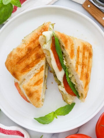 Overhead view of slices of Caprese Sandwich on a white plate with basil.