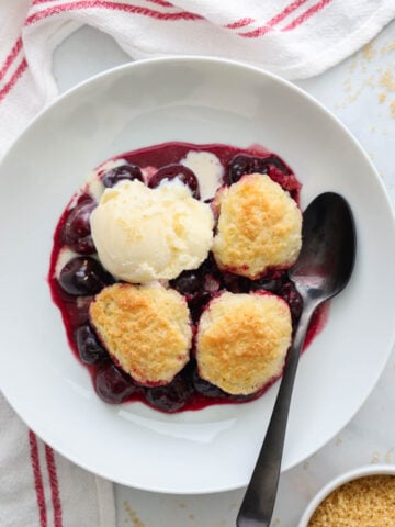 Cherry Cobbler on a white plate with a spoon and ice cream on top