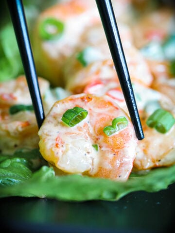 Grilled Bang Bang Shrimp on lettuce being picked up with chopsticks.