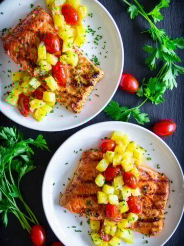 Pineapple Salmon on a plate with pineapple, cherry tomatoes, and chopped parsley on top.