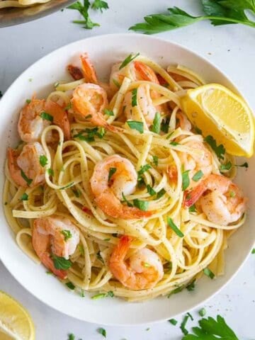 a close up of shrimp linguine in a white plate with lemons and parsley on top