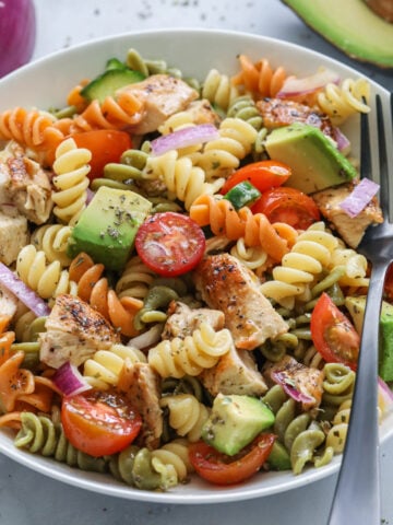 Chicken Pasta Salad with tomatoes, cucumber, avocado, rotini, and chicken in a bowl with a fork.