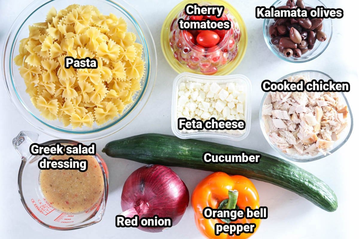 Ingredients for Greek Chicken Pasta Salad: pasta, cherry tomatoes, kalamata olives, cooked chicken, feta cheese, cucumber, orange bell pepper, red onion, and Greek salad dressing.