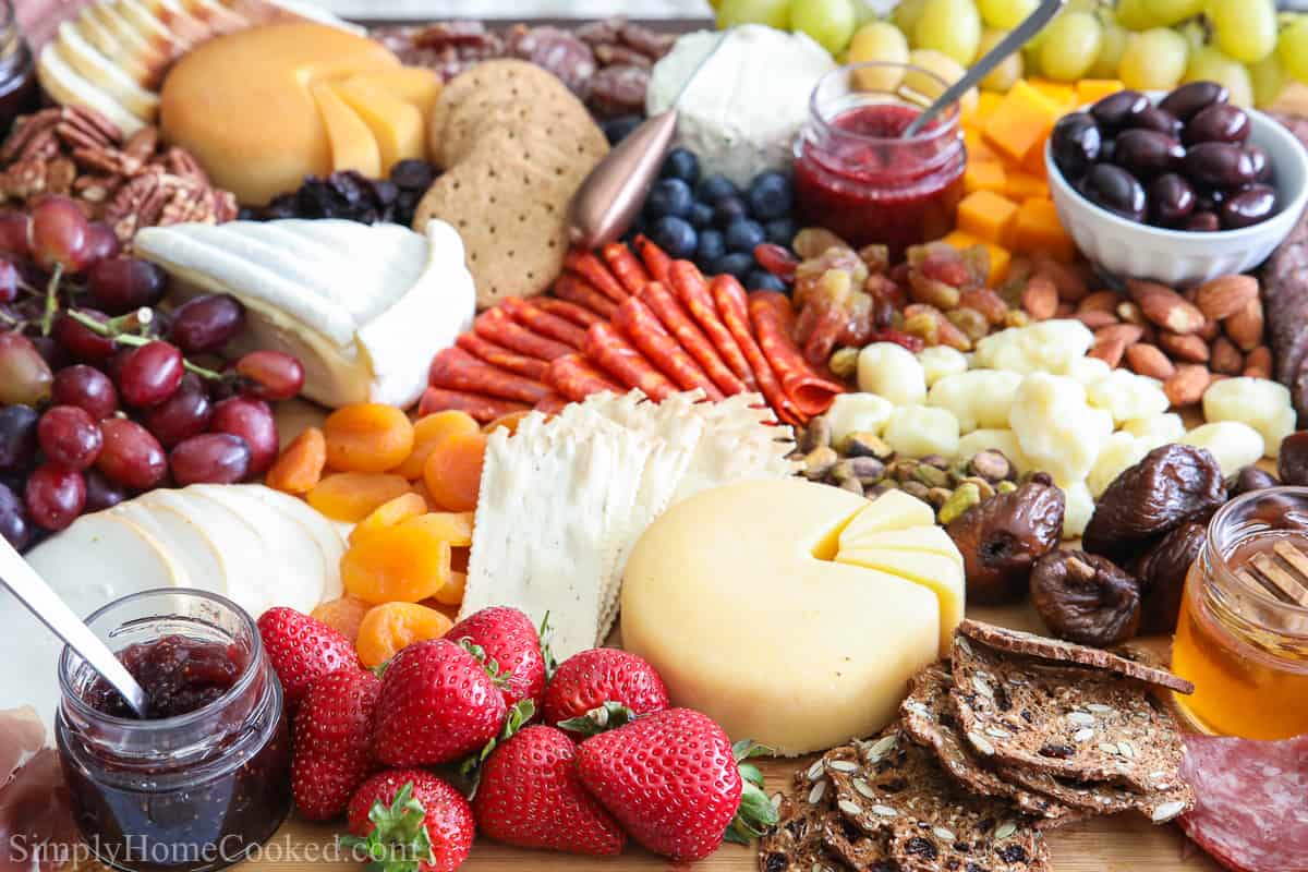 Close up of an Ultimate Charcuterie Board, including an assortment of meats, cheeses, fruit, nuts, olives, jams, breads, crackers, and honey.