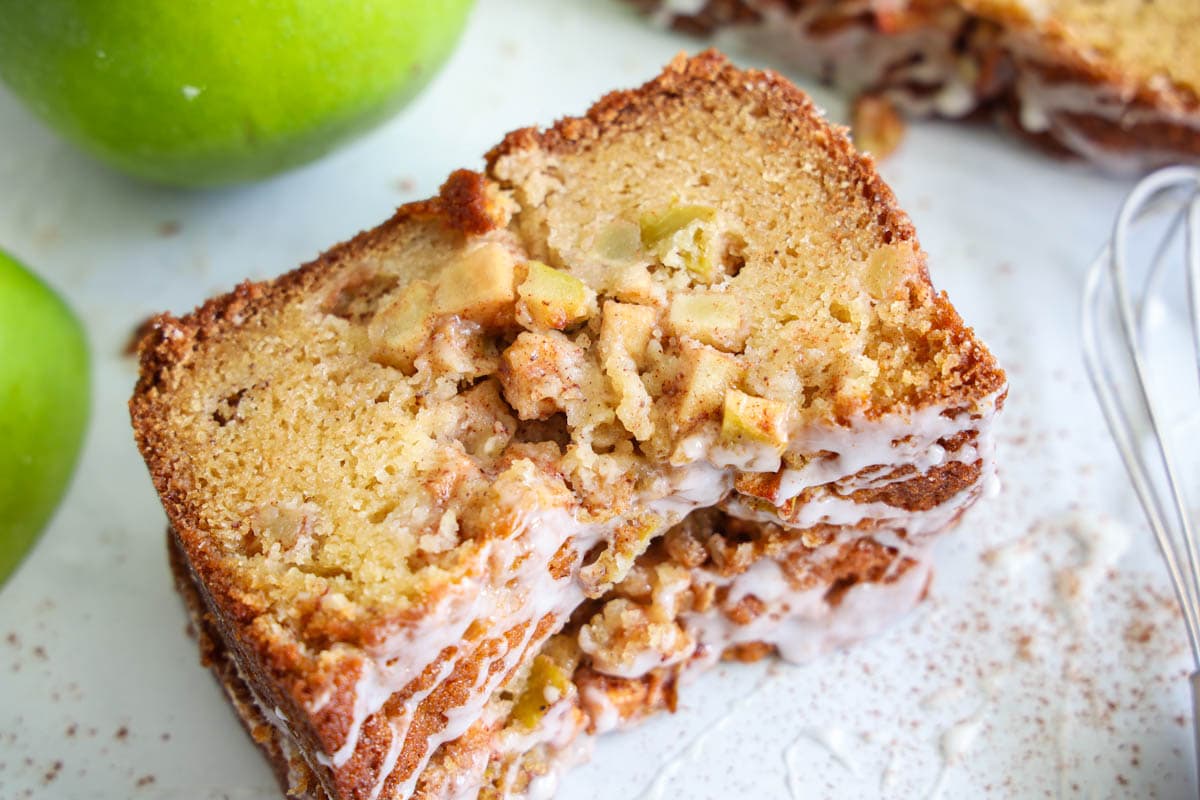 Slices of Apple Fritter Bread with apples and a whisk nearby.