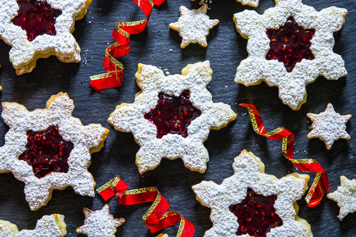 Linzer Cookies with Raspberry Jam dusted with powdered sugar with ribbons nearby.