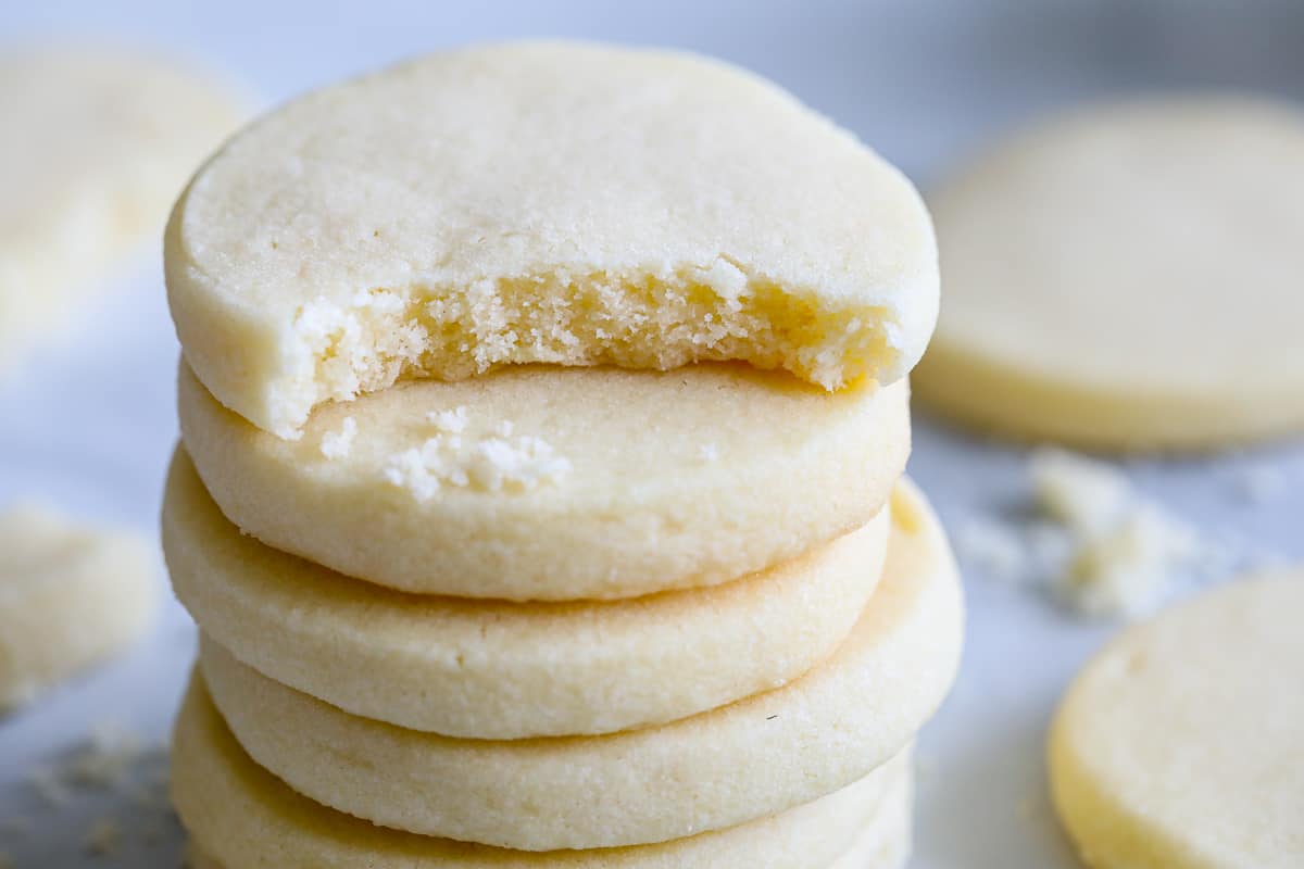 Stack of Classic Shortbread Cookies with a bite missing from the top one and more cookies in the background.