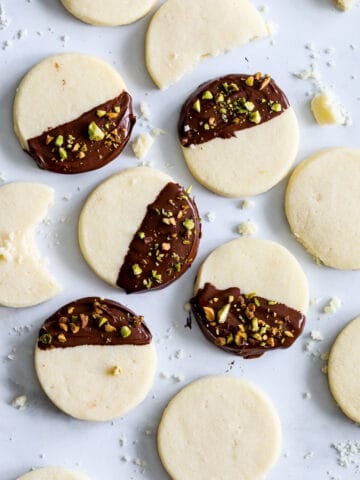 Tray of Classic Shortbread Cookies, some dipped in chocolate and sprinkled with chopped pistachios, with some crumbs in the background.
