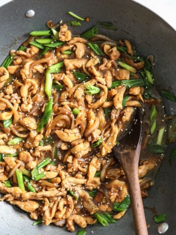 Closeup of Easy Mongolian Chicken in a wok with a wooden spoon.