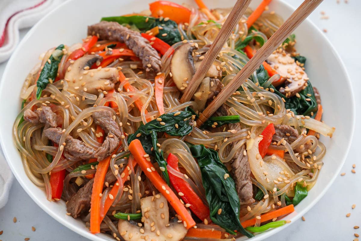 Easy Japchae in a white bowl with chopsticks.