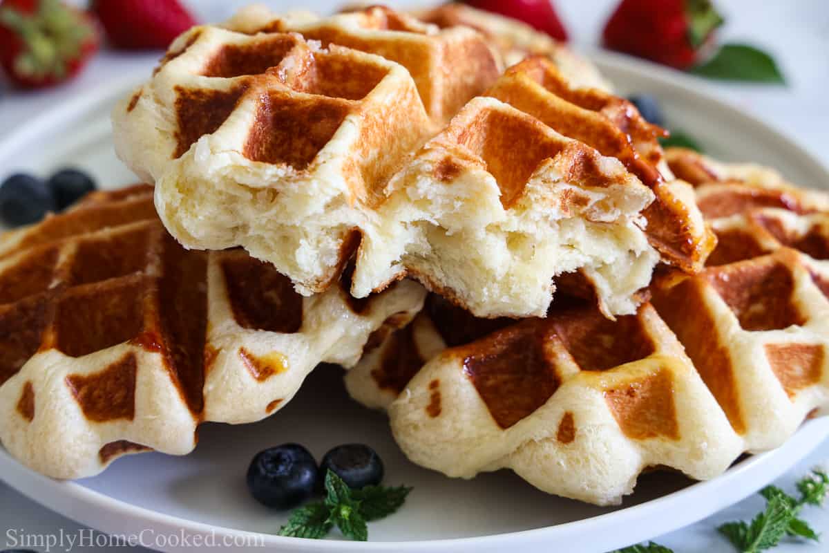 Close up of Buttery Belgian Liege Waffle with blueberries, strawberries, and mint leaves in the background.