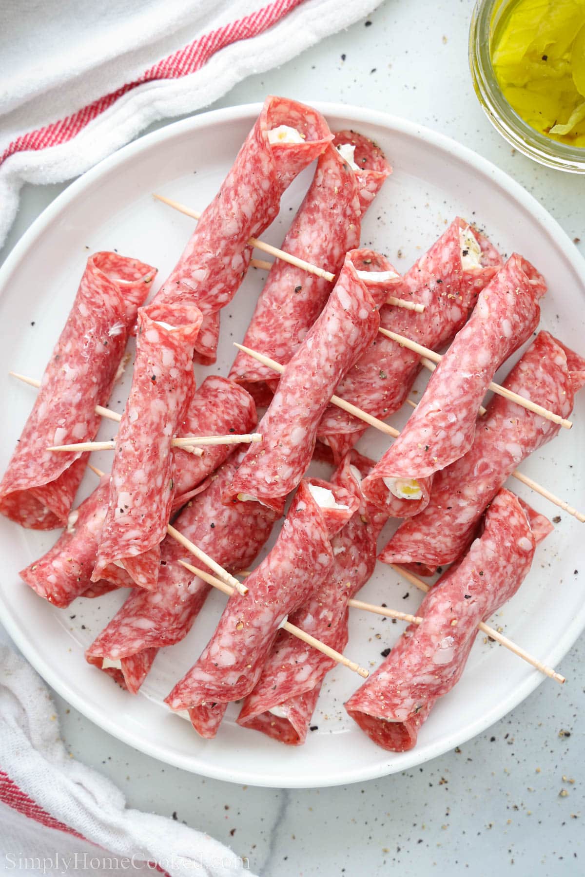 Overhead of plate of Salami Roll-Ups with pepperoncini nearby.