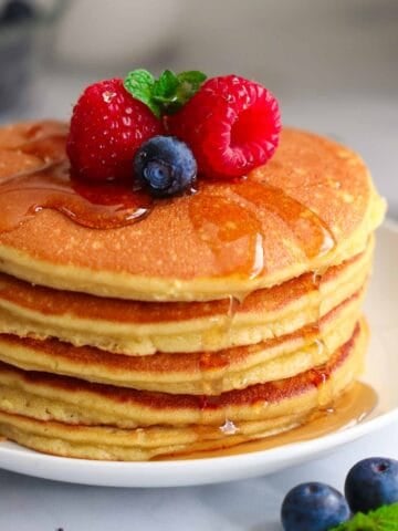 Stack of Almond Flour Pancakes with raspberries, blueberries, and mint on top with syrup.