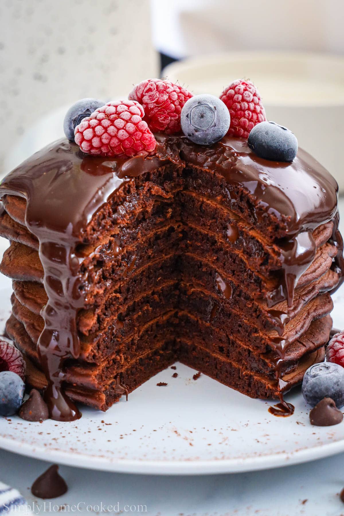 Stack of Chocolate Pancakes topped with chocolate ganache and berries, a piece missing.