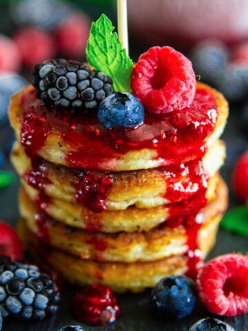 Vertical image of a stack of Cottage Cheese Pancakes with raspberry sauce and fresh berries.