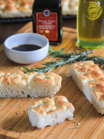 Focaccia Bread slices on a cutting board with rosemary sprigs, oil, and balsamic vinegar.